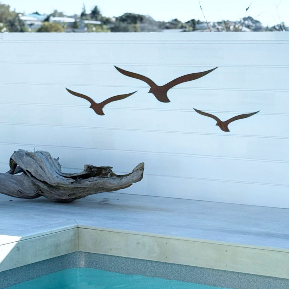 NZ-made corten bird wall art mounted on white exterior near pool.