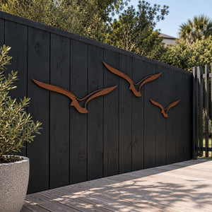 Set of three Corten steel albatross wall art pieces in flight, mounted outdoors on a fence in an Auckland garden