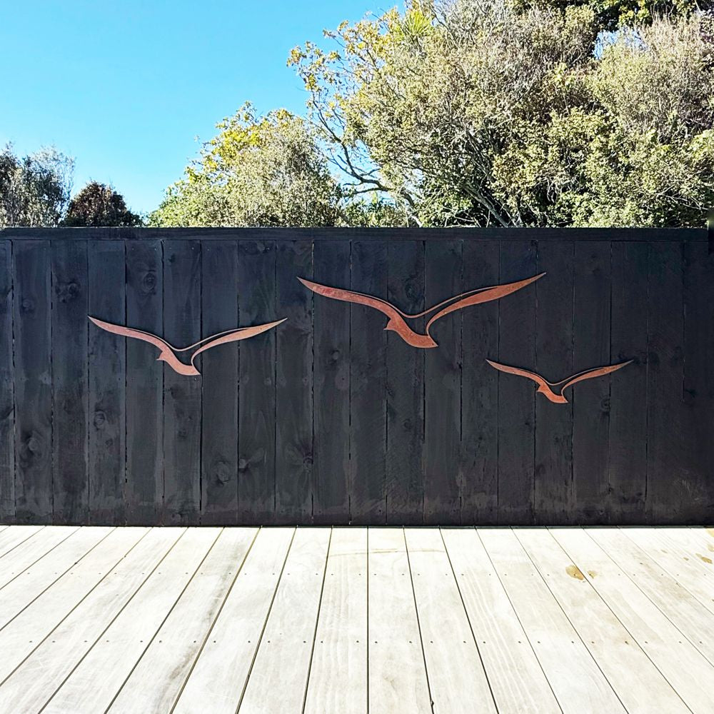 Set of three Corten steel albatross wall art pieces in flight, mounted outdoors on a fence in an Auckland garden