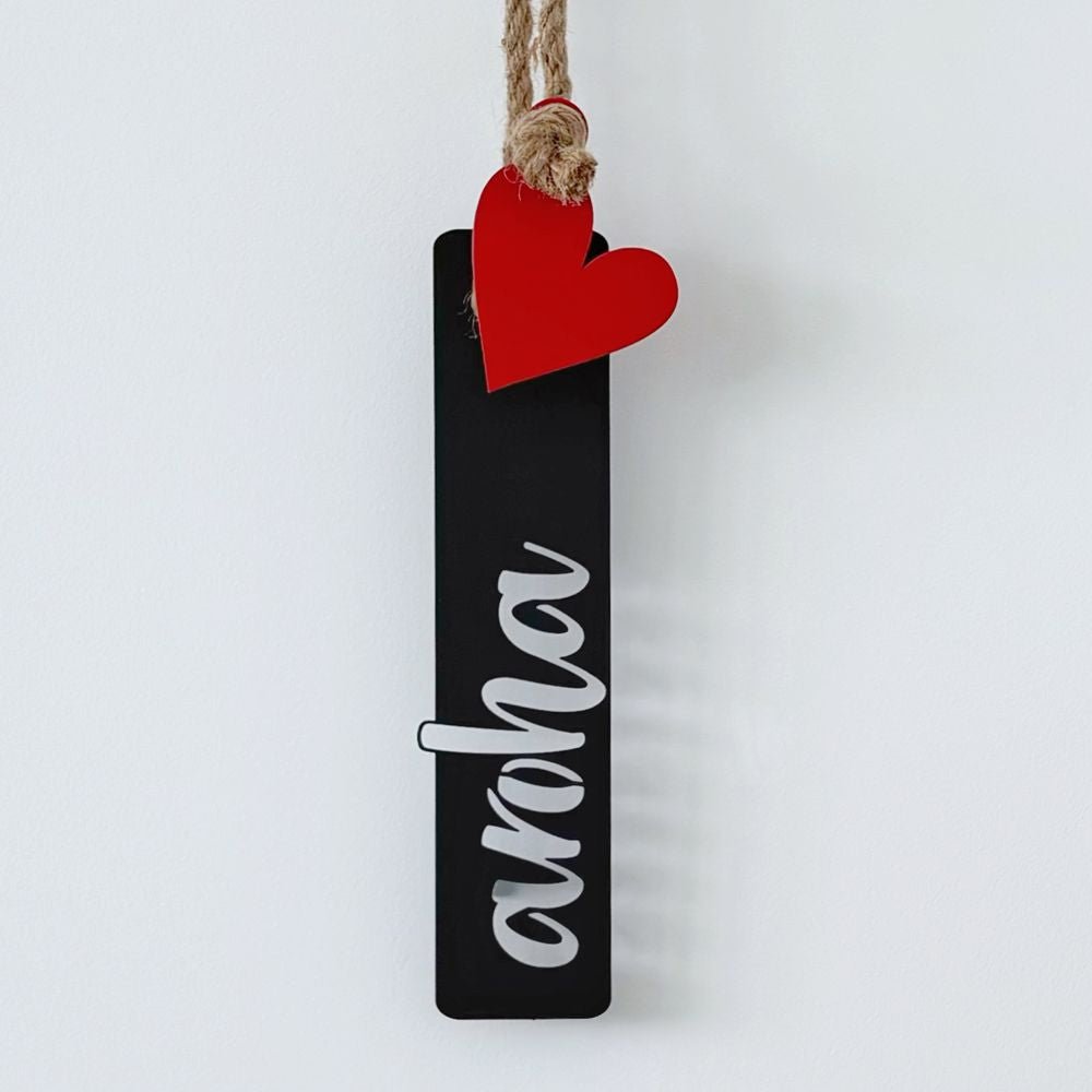 Decorative aroha love hanging sign with a red heart and black rectangle on a white wall next to a framed abstract art print.