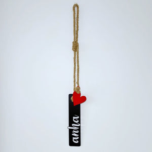 Black rectangular tag with 'aroha' text and red heart, hanging on a rope against a white background