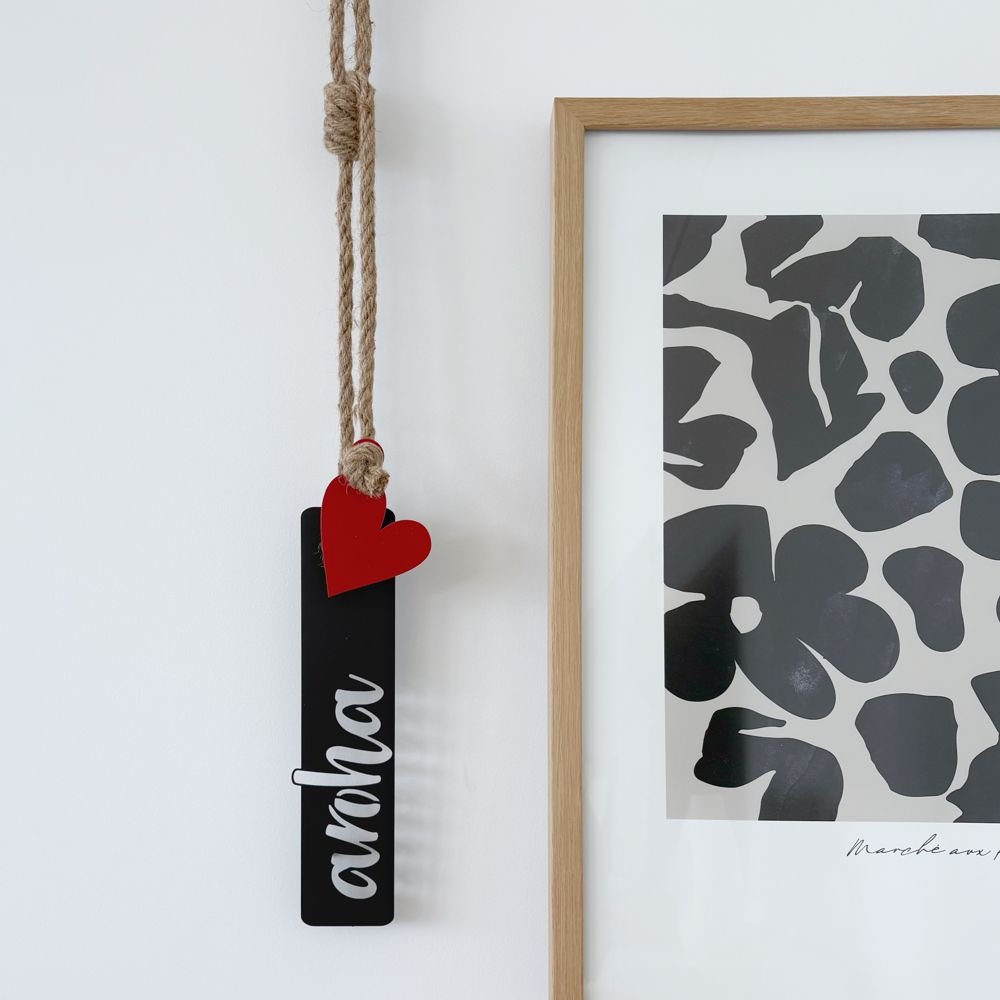 Decorative aroha love hanging sign with a red heart and black rectangle on a white wall next to a framed abstract art print.