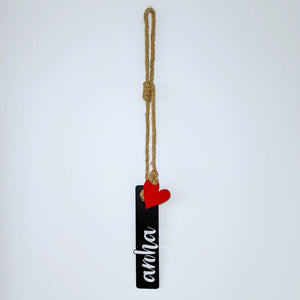 Black rectangular tag with 'aroha' text and red heart, hanging on a rope against a white background