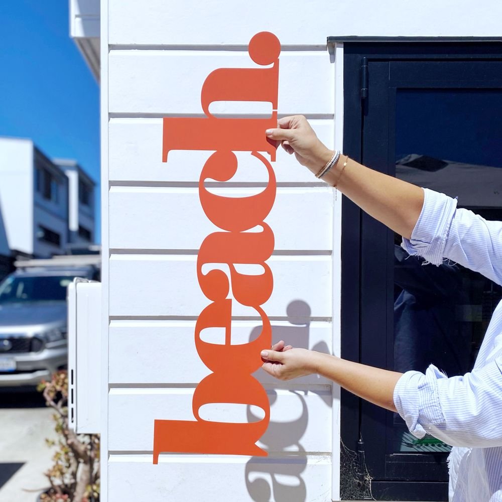 Orange beach decor on wall in modern coastal New Zealand home with tropical planting. 