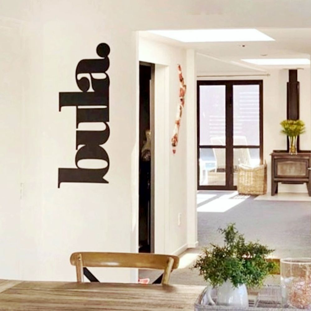 A modern interior scene with a large black custom metal wall art spelling 'bula.' in a stylized vertical font on an off-white wall.