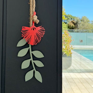 Decorative metal wall art with red flower and green leaves on a black background, poolside setting.
