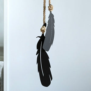 Black feather-shaped wall decor hanging on a rope against a wall in a New Zealand home 