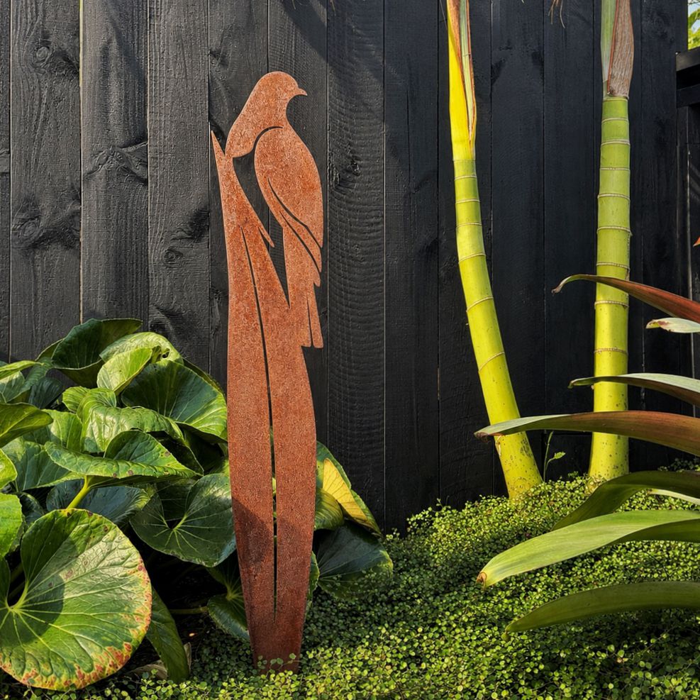 Rusted corten steel kereru on flax garden stake, 90cm tall, planted in a New Zealand garden border