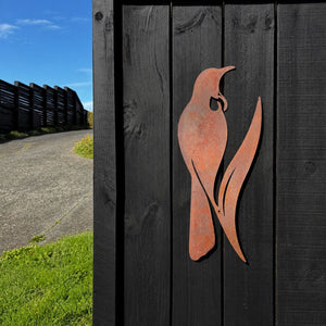 Rusted corten tui silhouette on a timber fence in a New Zealand garden
