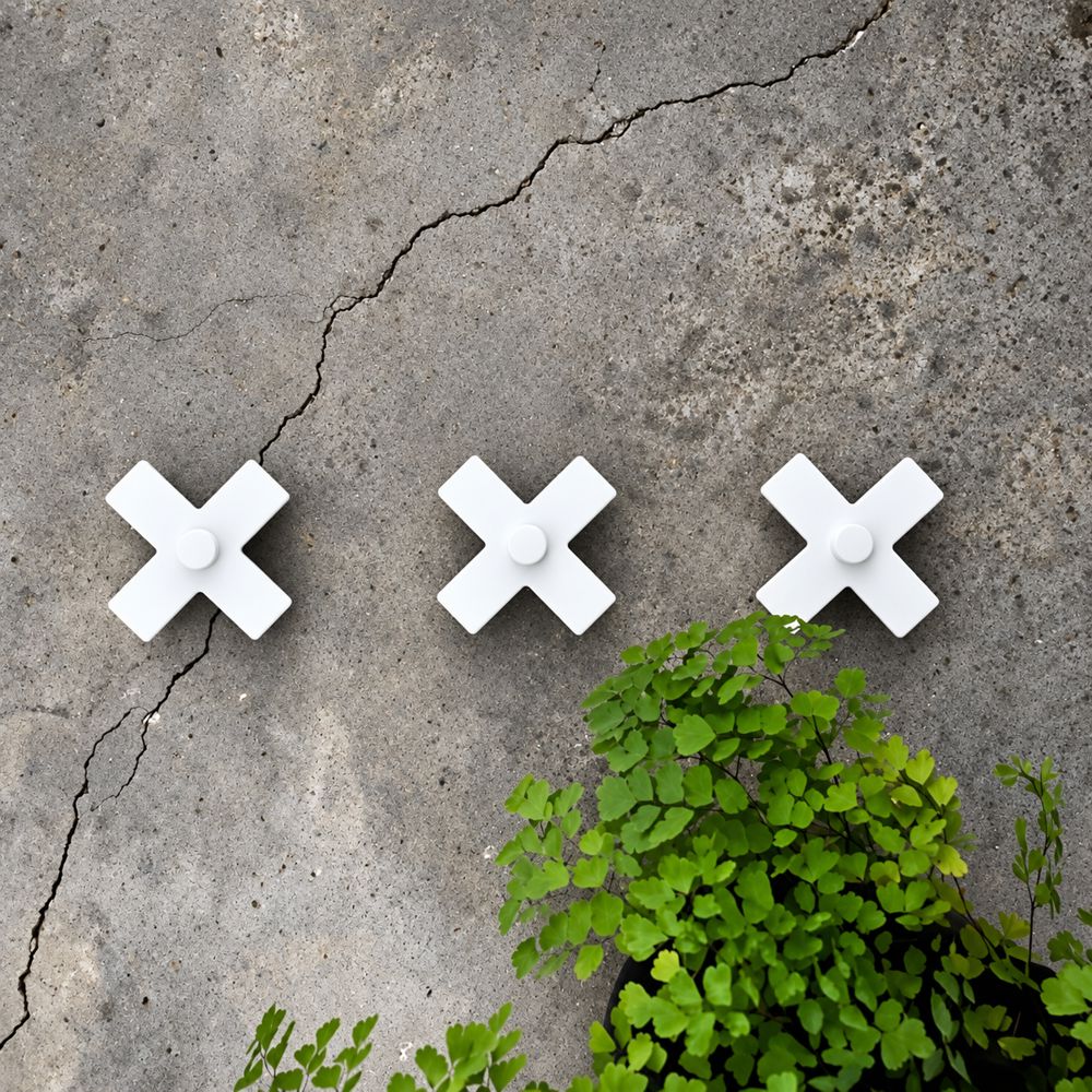 Matte white decorative steel cross wall hooks on concrete wall in garden. 