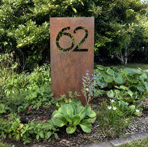 Large custom corten steel house number garden stake outside a rural New Zealand home, modern rusted steel address sign in landscaped front garden