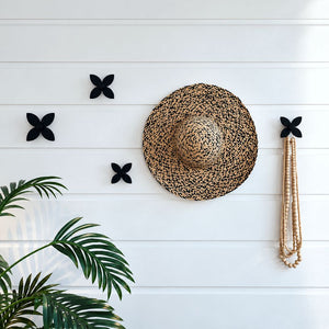 Five matte black steel frangipani wall hooks holding hait and jewellery in an entryway.