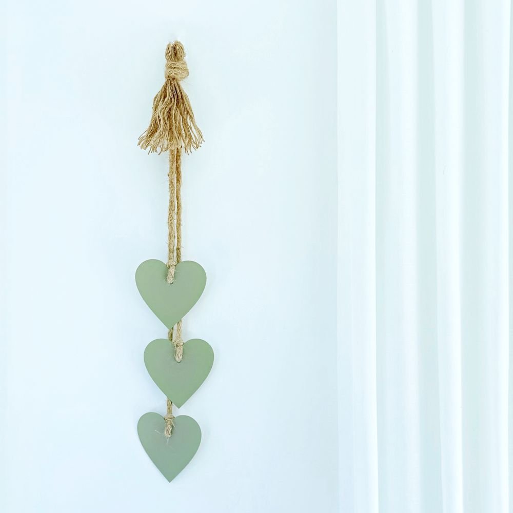 Decorative hanging with three green hears and a tassel on a white wall in a New Zealand home. 
