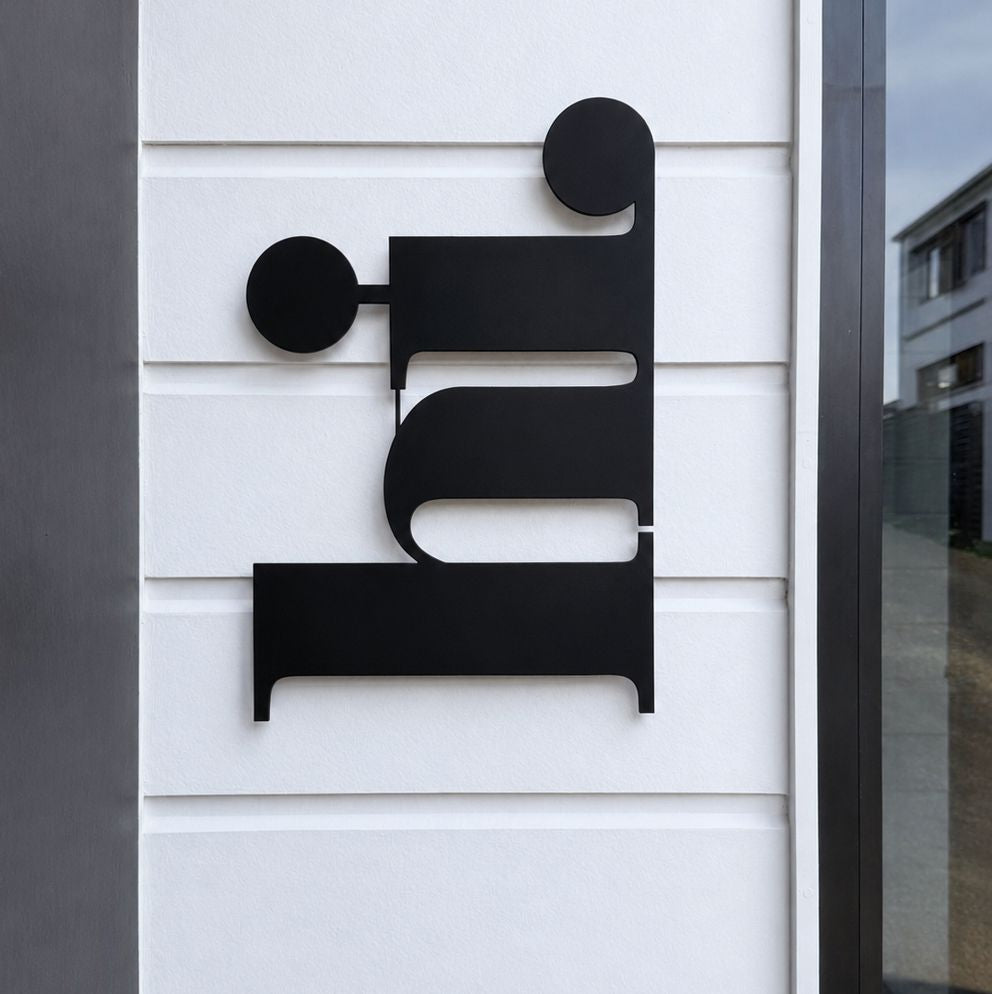 A modern black metal wall art piece mounted on a white horizontal-siding exterior wall.