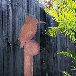Close-up of rusted corten kingfisher garden art stake with native NZ garden in background