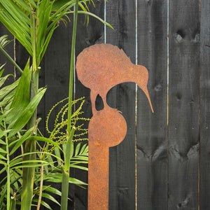 Close-up of rusted kiwi garden art stake with native NZ foliage behind. 