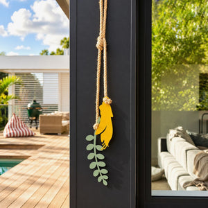 Yellow kowhai flower wall hanging on natural rope, styled on a black outdoor wall by a deck and pool