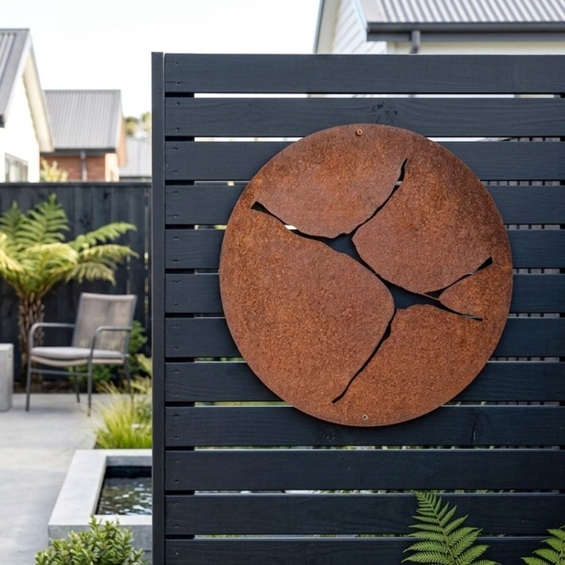 Large round corten steel outdoor wall art on black fence of modern NZ home