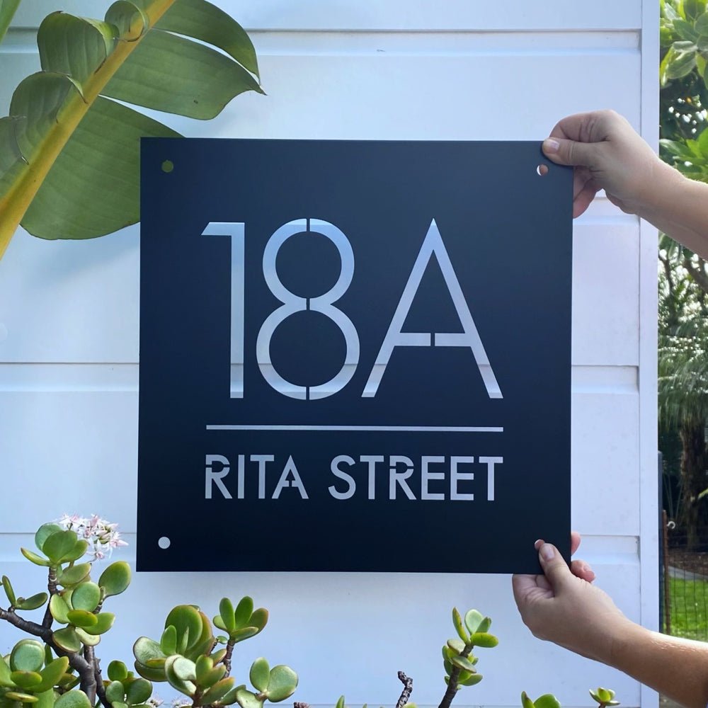 Front-on view of large square house number sign in matte black powdercoated steel mounted on exterior wall