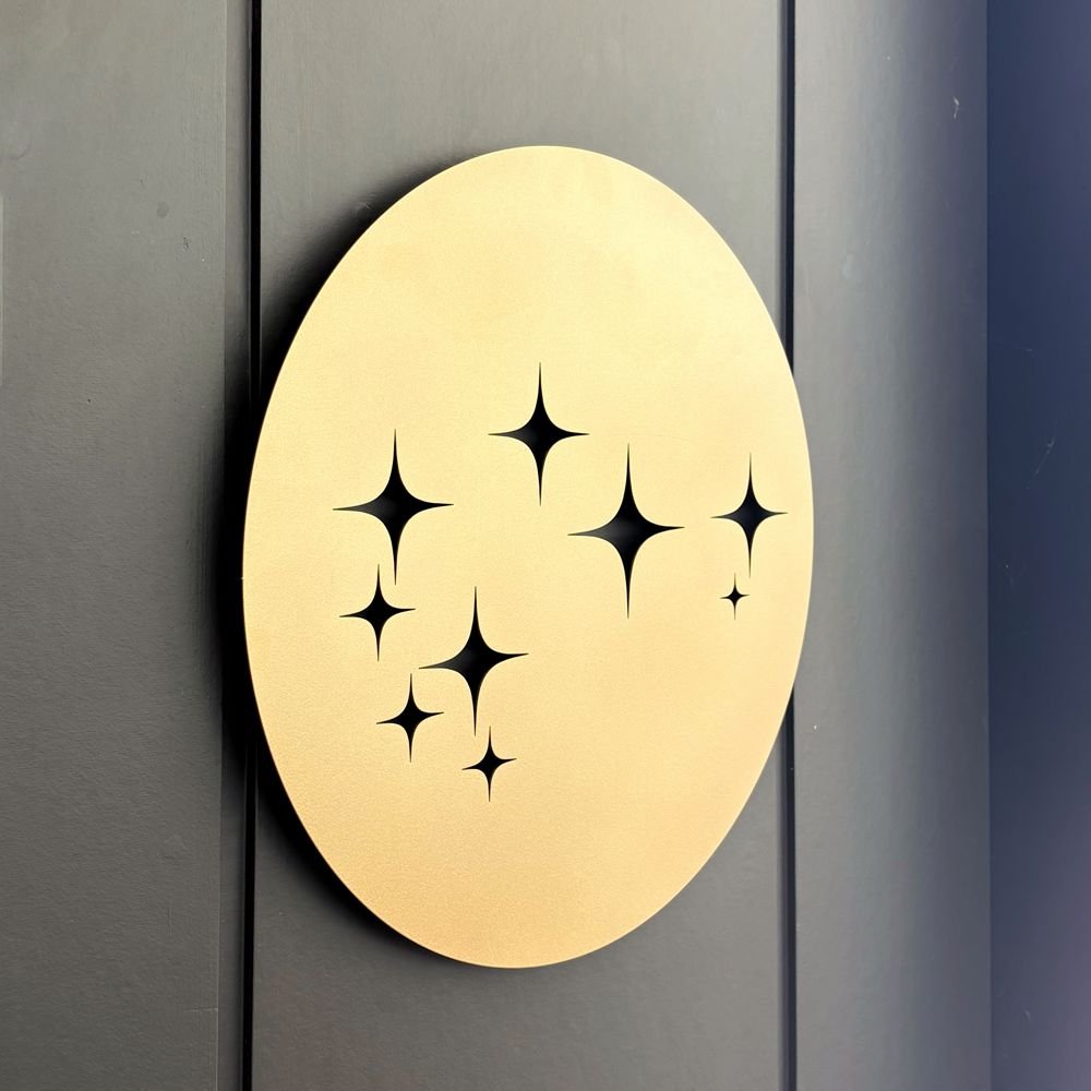 Matte gold Matariki round steel wall art displayed on a black wall in a modern New Zealand outdoor patio, suitable for indoor and outdoor use