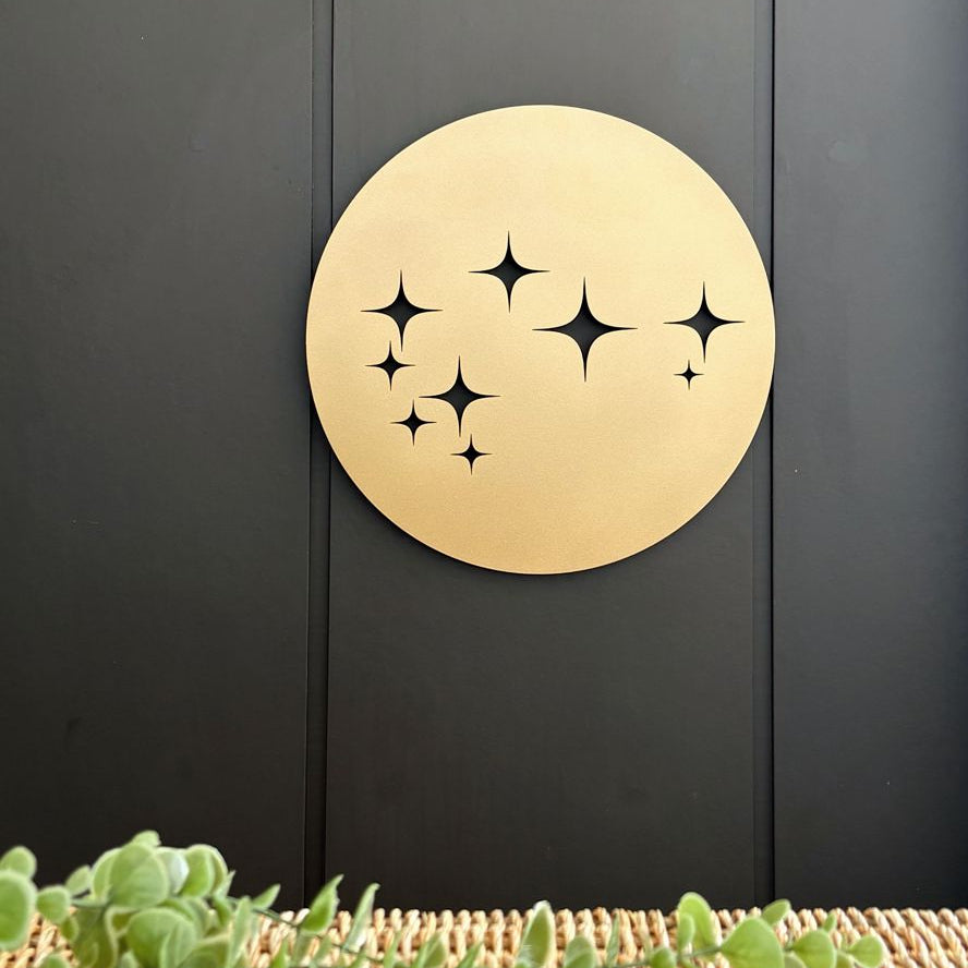 Matte gold Matariki round steel wall art displayed on a black wall in a modern New Zealand outdoor patio, suitable for indoor and outdoor use