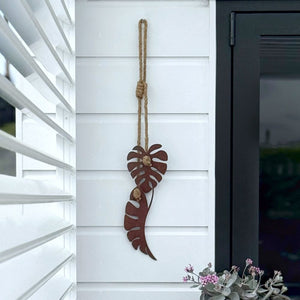 Decorative monstera leaft corten wall art hanging on a white wall with a black door.