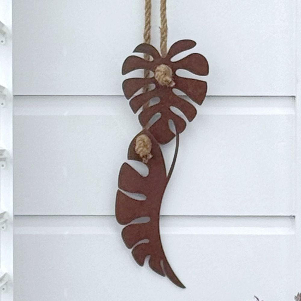 Decorative monstera leaft corten wall art hanging on a white wall with a black door.