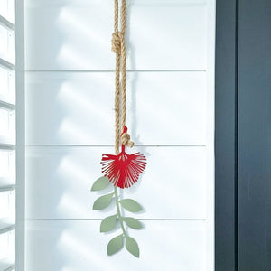 Red Pohutukawa flower garden ornament hanging from a rope on a white wall.