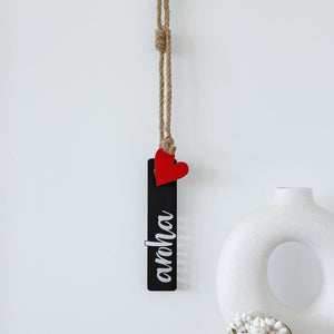 Black rectangular sign with a red heart and 'aroha' text, hanging on a white background. LisaSarah