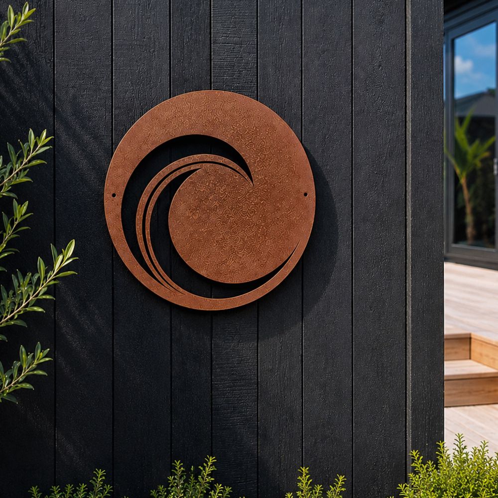 Round 50cm corten steel wave wall art mounted on a black fence in a New Zealand garden.
