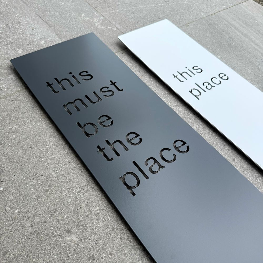 Matte charcoal “This Must Be The Place” metal wall art installed outdoors on exterior wall