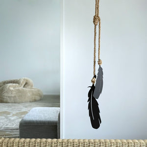 Black tui feather outdoor wall ornament hanging from a rope against a white wall.