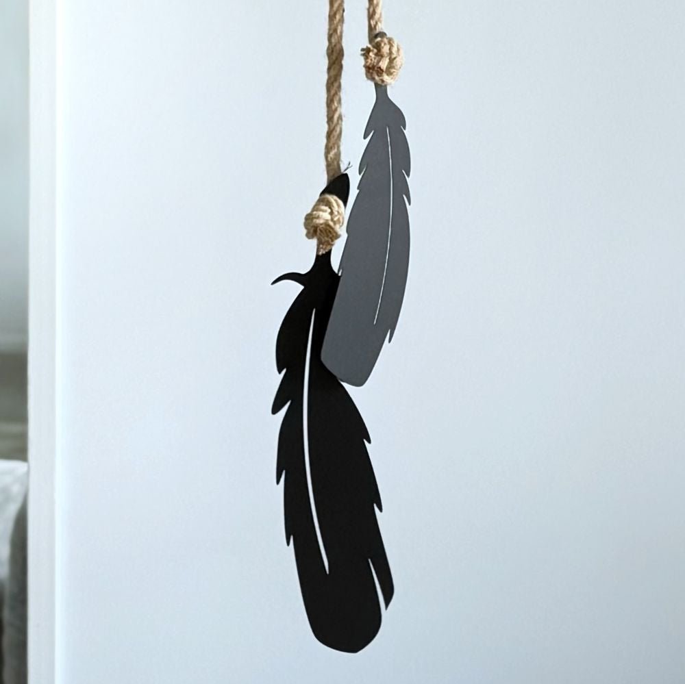 Decorative tui feathers hanging from a rope against a white wall.