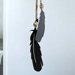 Black feather-shaped wall decor hanging on a rope against a wall in a New Zealand home 