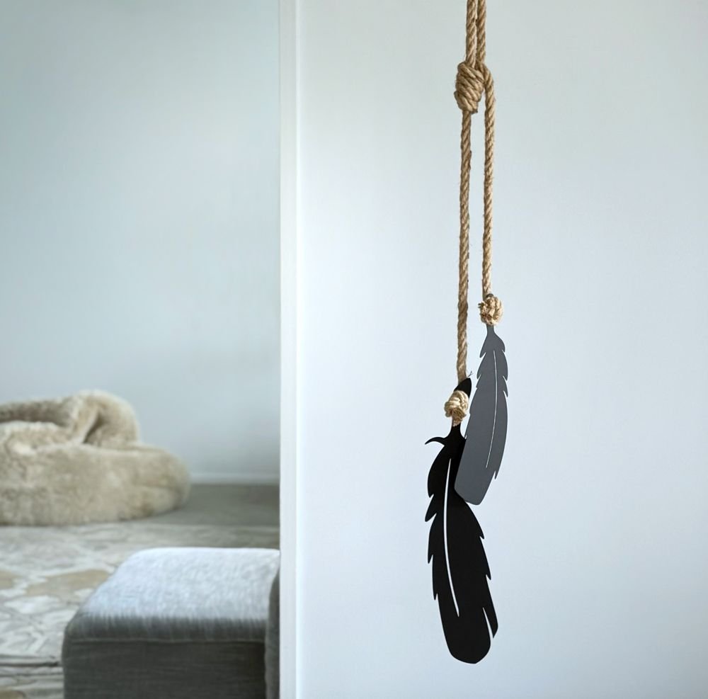 Decorative tui feathers hanging from a rope against a white wall.