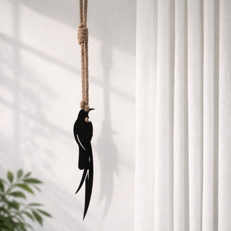 tui-shaped ornament hanging from a rope against a white curtain background